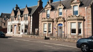 A row of traditional stone buildings with distinct architectural features, including multiple chimneys and arched windows. - Ardross Glencairn (Inverness)