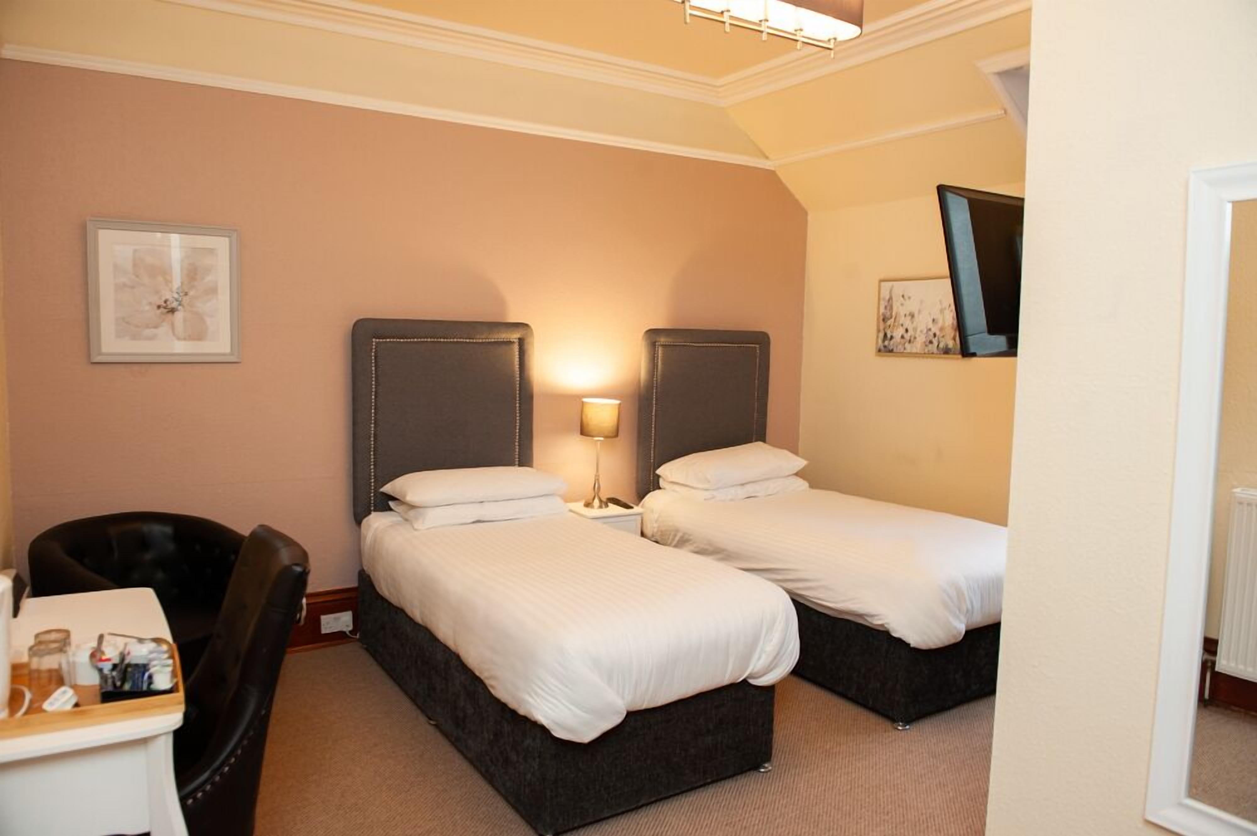 A hotel room with two beds, a desk with a chair, a lamp, and artwork on the walls.