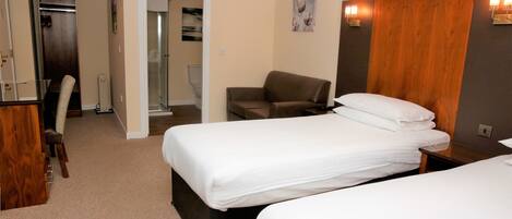 A hotel room with two beds, a wooden headboard, a chair, and a desk.