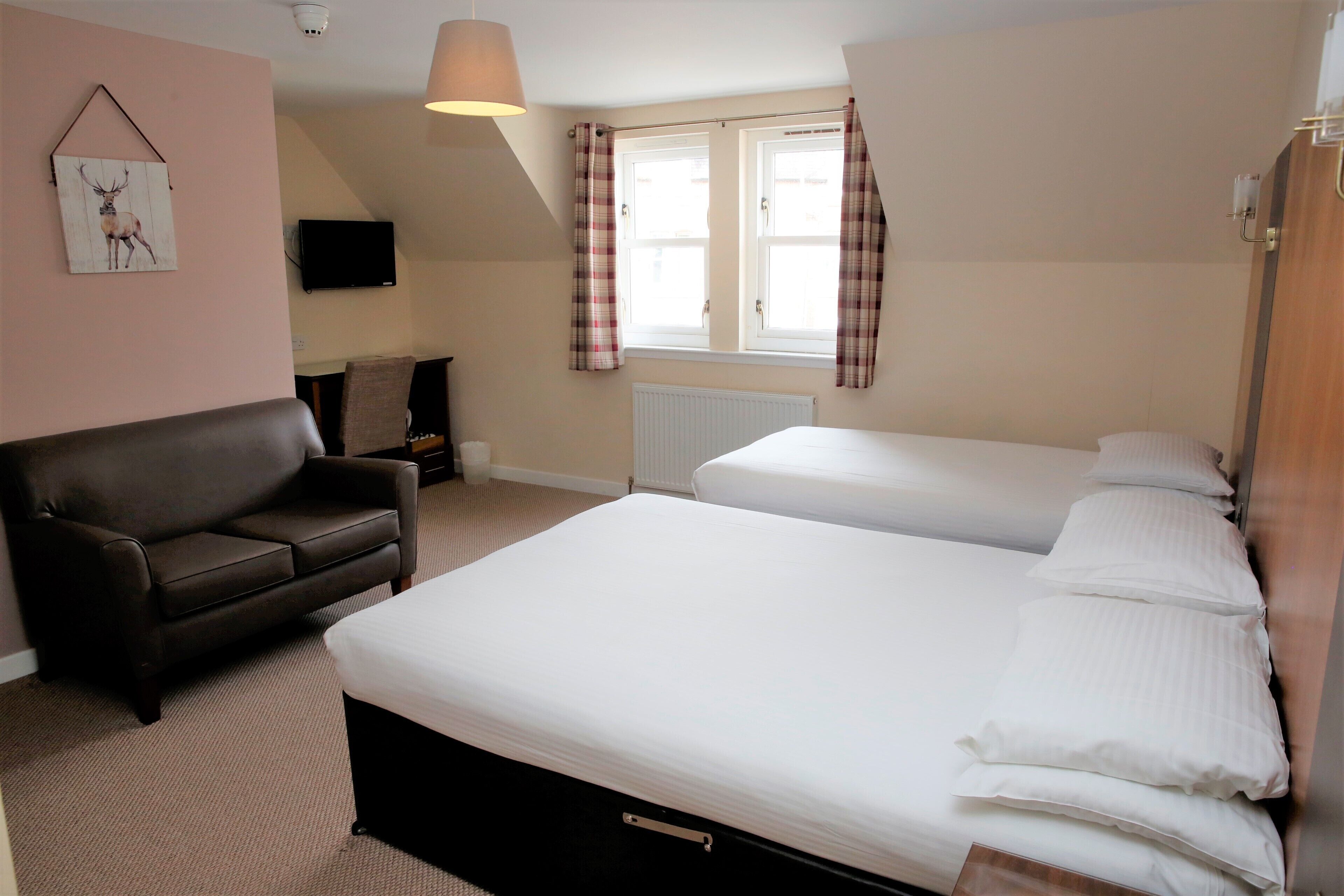 A hotel room with two beds, a sofa, a TV, and a window with curtains.
