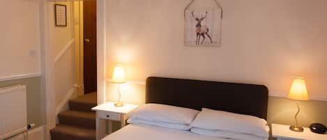 A bedroom with a bed, two bedside tables with lamps, a framed deer picture on the wall, and a staircase leading to another room.
