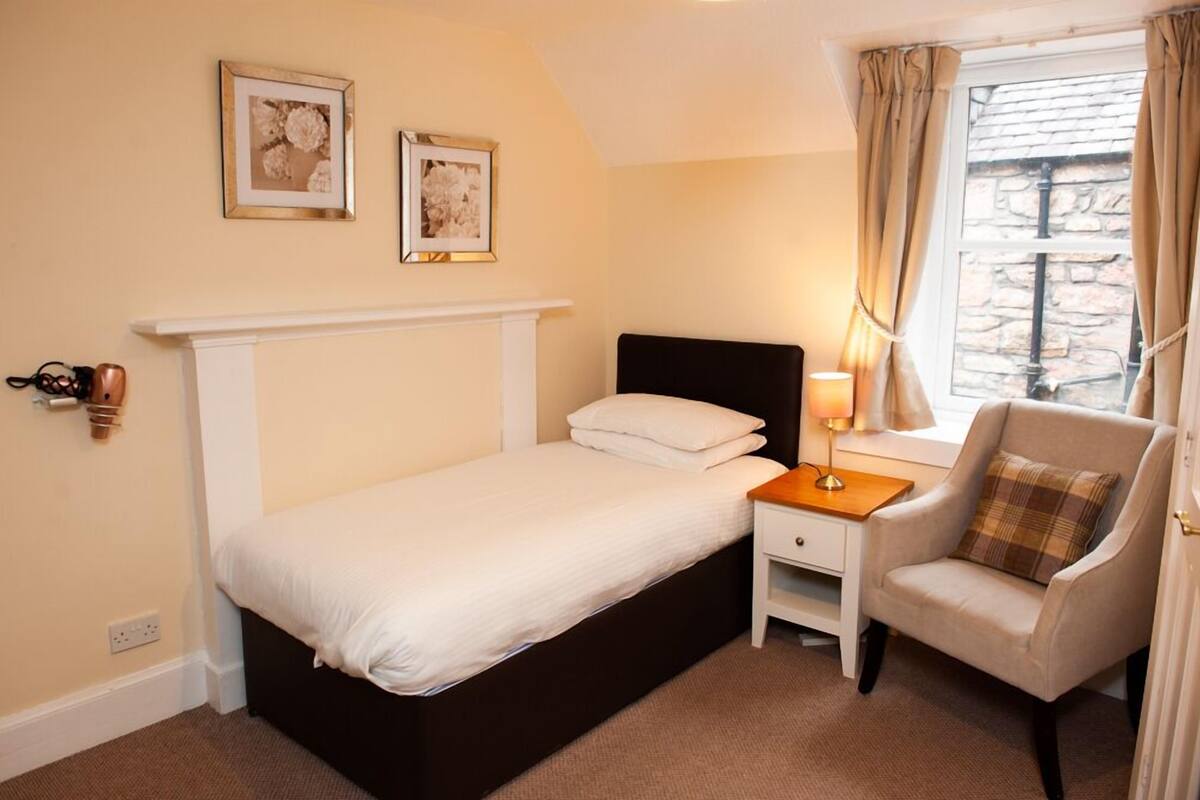 A bedroom with a bed, a nightstand, a chair, and a window with curtains.