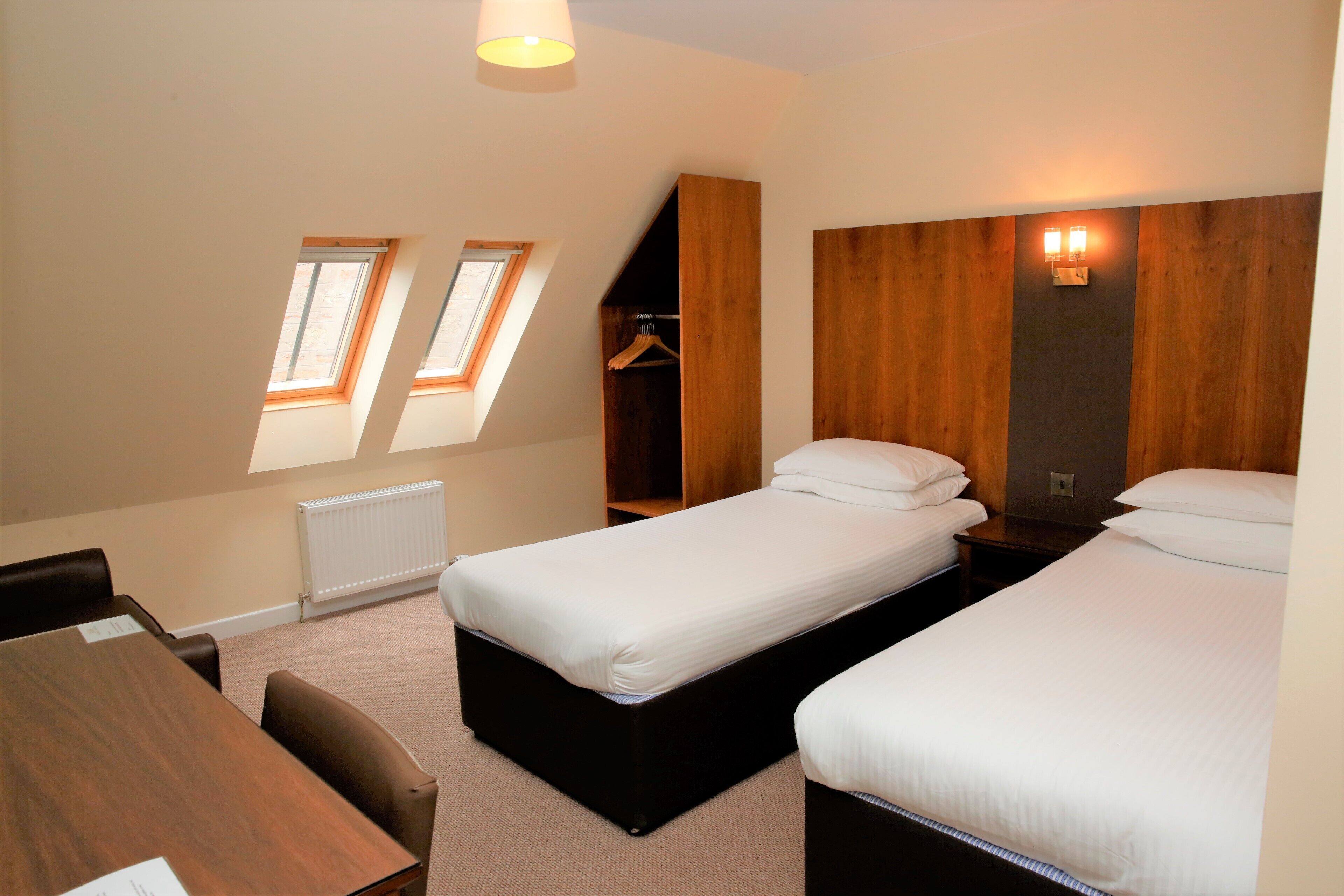 Ein Hotelzimmer mit zwei Betten, einem Schreibtisch und einem Kleiderschrank. Es gibt Dachfenster und eine Heizung.