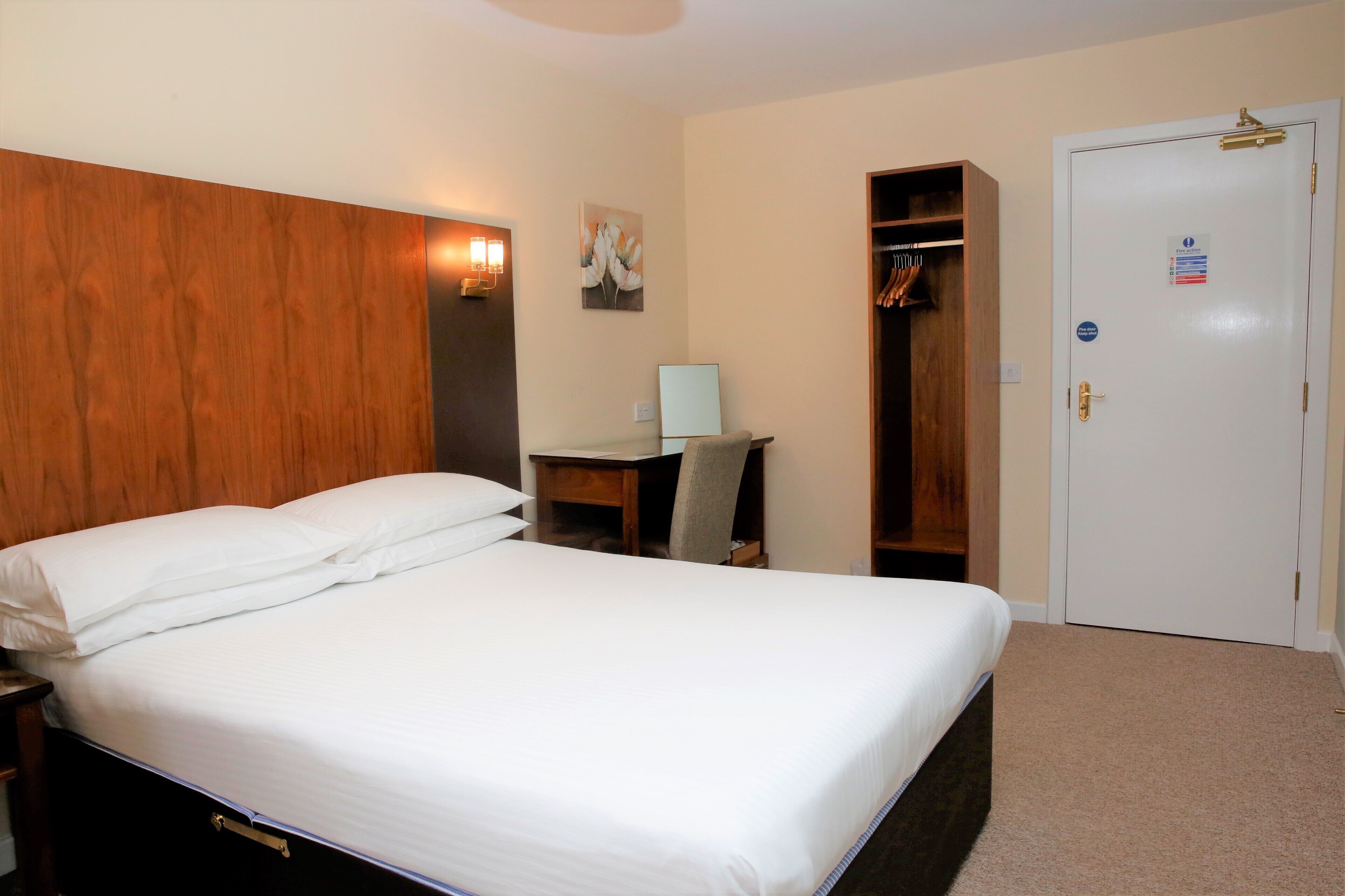 Une chambre d’hôtel avec un lit, un bureau, une chaise, une armoire et une porte.
