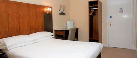 A hotel room with a bed, a desk, a chair, a wardrobe, and a door.