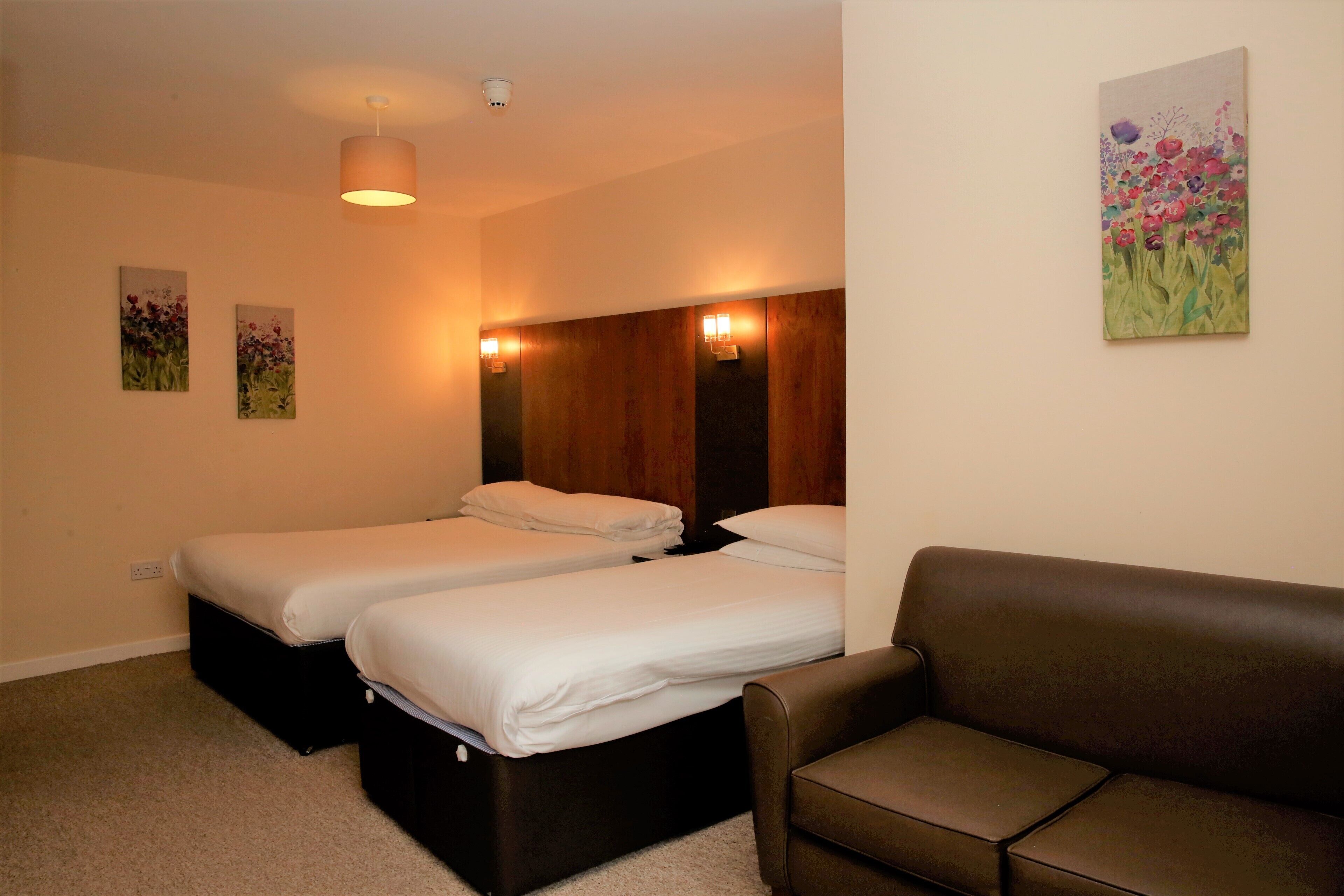 Ein Hotelzimmer mit zwei Einzelbetten, einem braunen Ledersofa und einem Bild an der Wand.