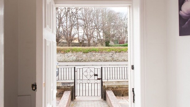 A white door with a number '18' above it, leading to a gated entrance with a stone wall and a paved path. - Ardross Glencairn (Inverness)