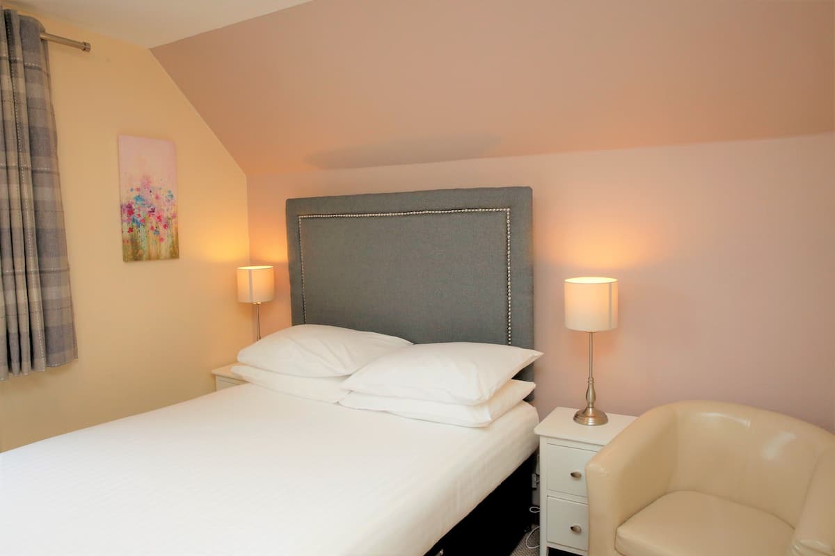 A neatly made bed with white linens and a grey upholstered headboard, flanked by two bedside lamps on a white nightstand.