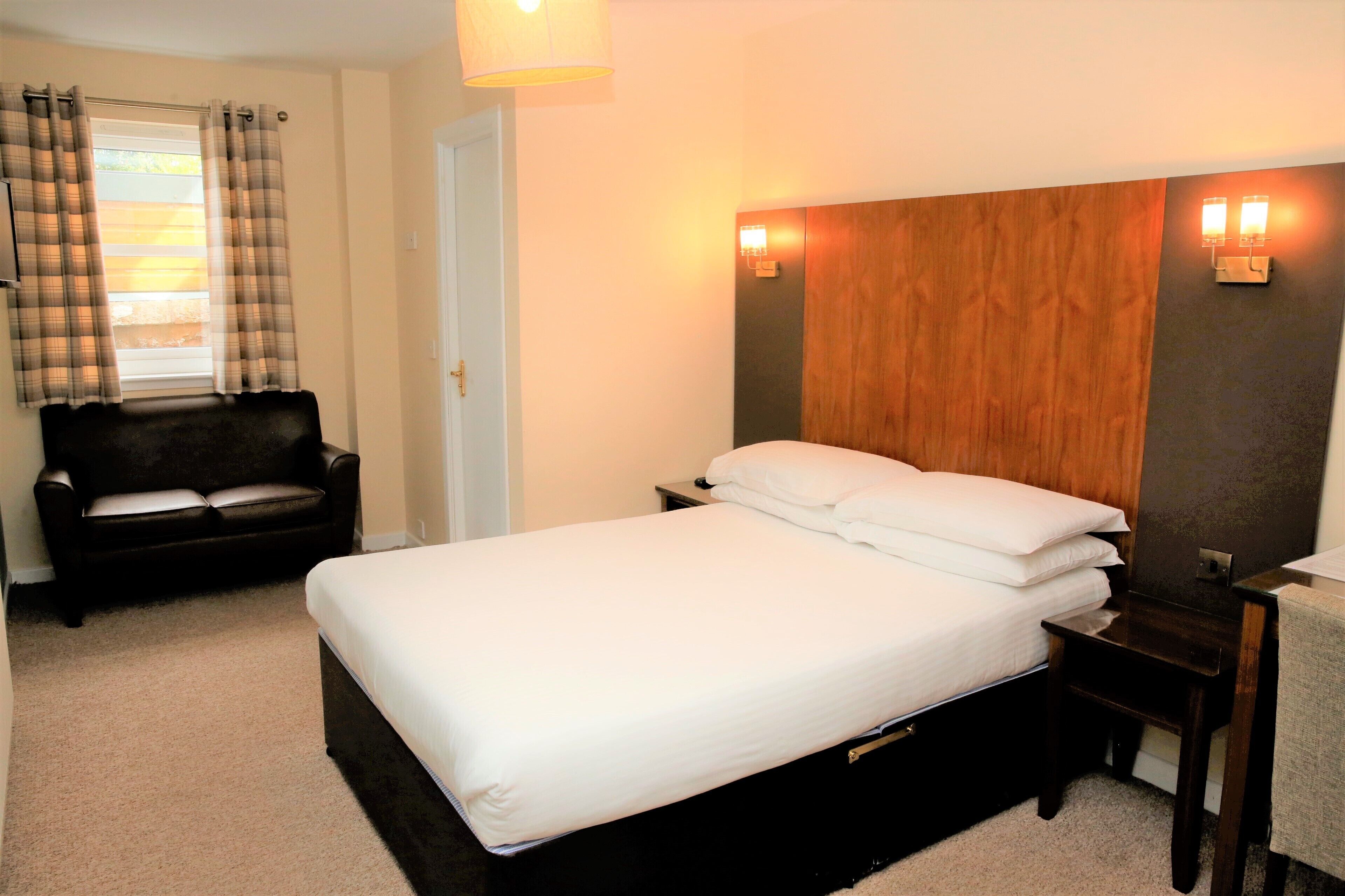 Une chambre d’hôtel avec un lit, une table de chevet, un bureau, une chaise et une fenêtre avec des rideaux.