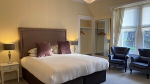 A bedroom with a large bed, two bedside lamps, a mirror, a wardrobe, and two armchairs. - Ardross Glencairn (Inverness)