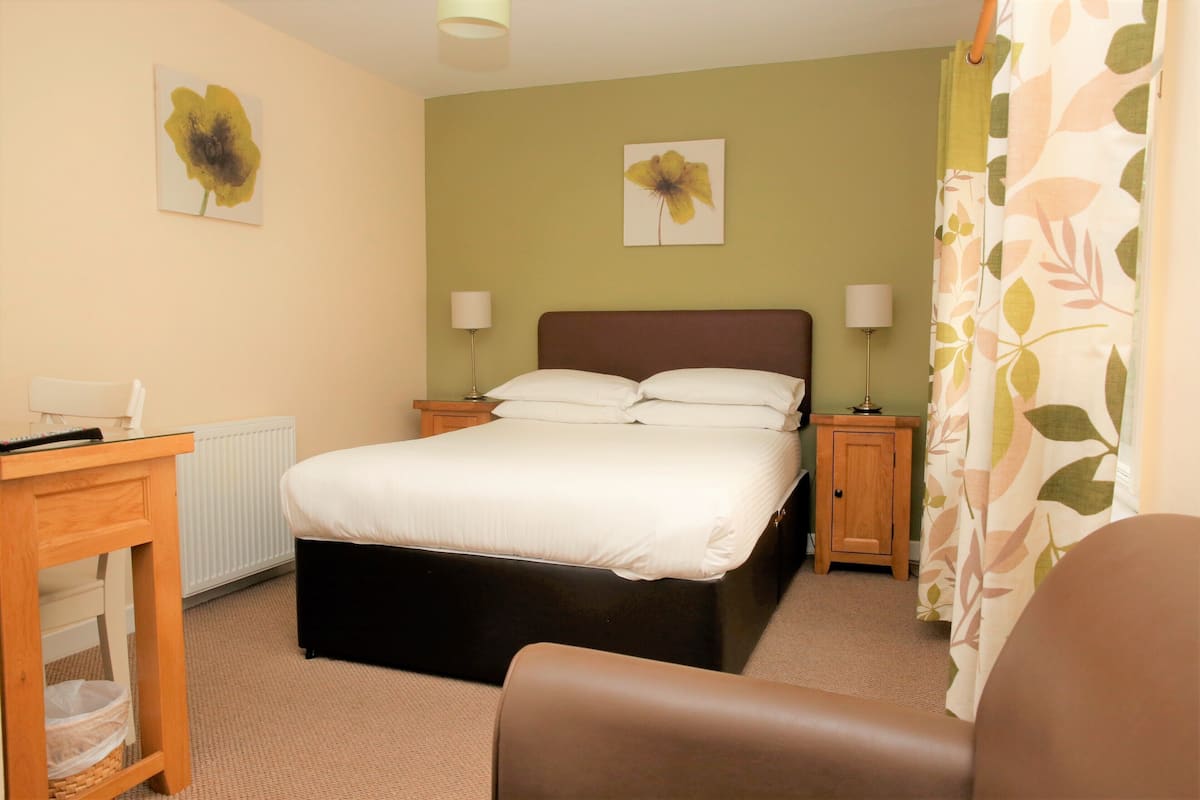 A bedroom with a bed, two bedside tables with lamps, a desk with a chair, and a radiator.