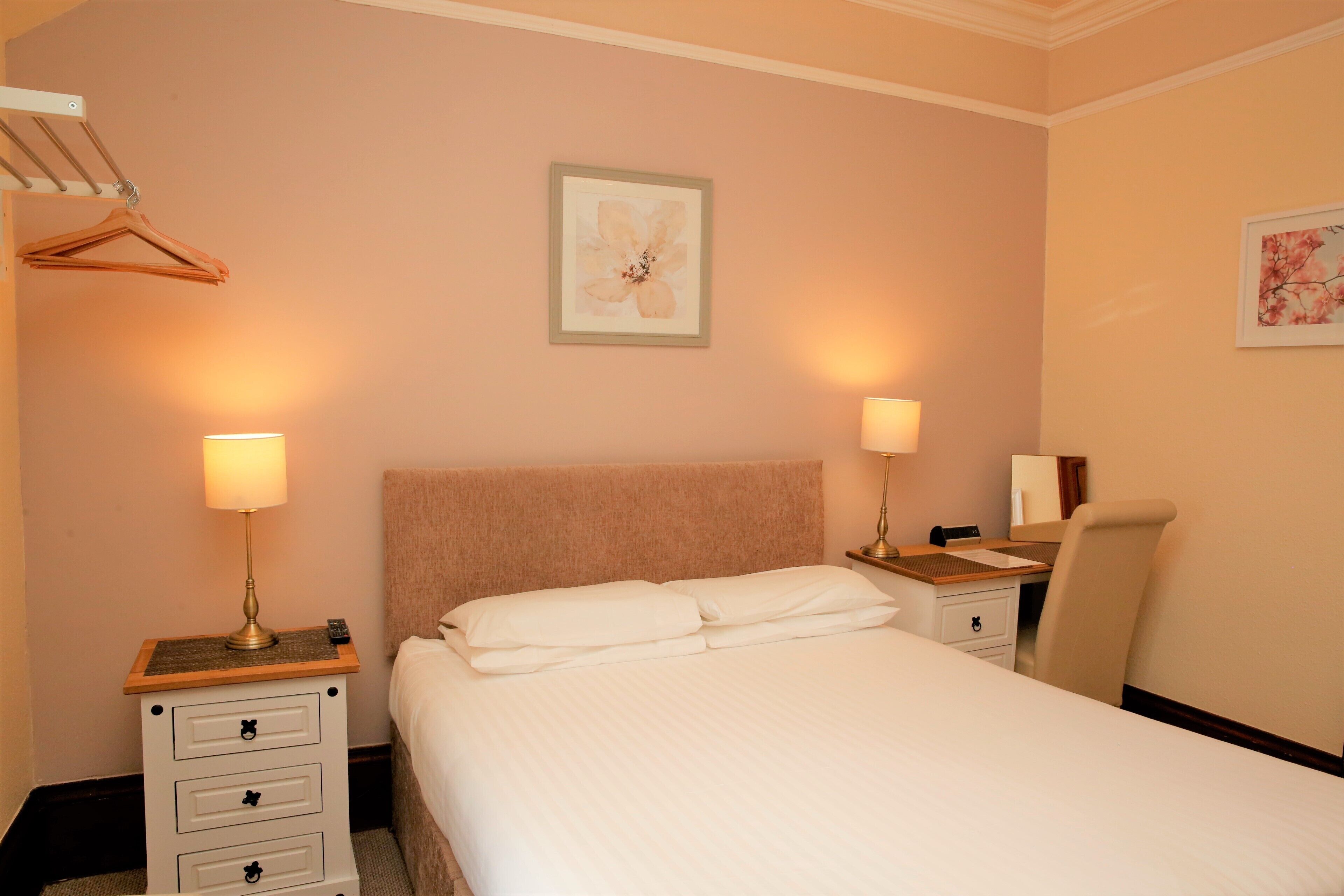 A hotel room with a large bed, two bedside tables with lamps, a chair, and a desk.