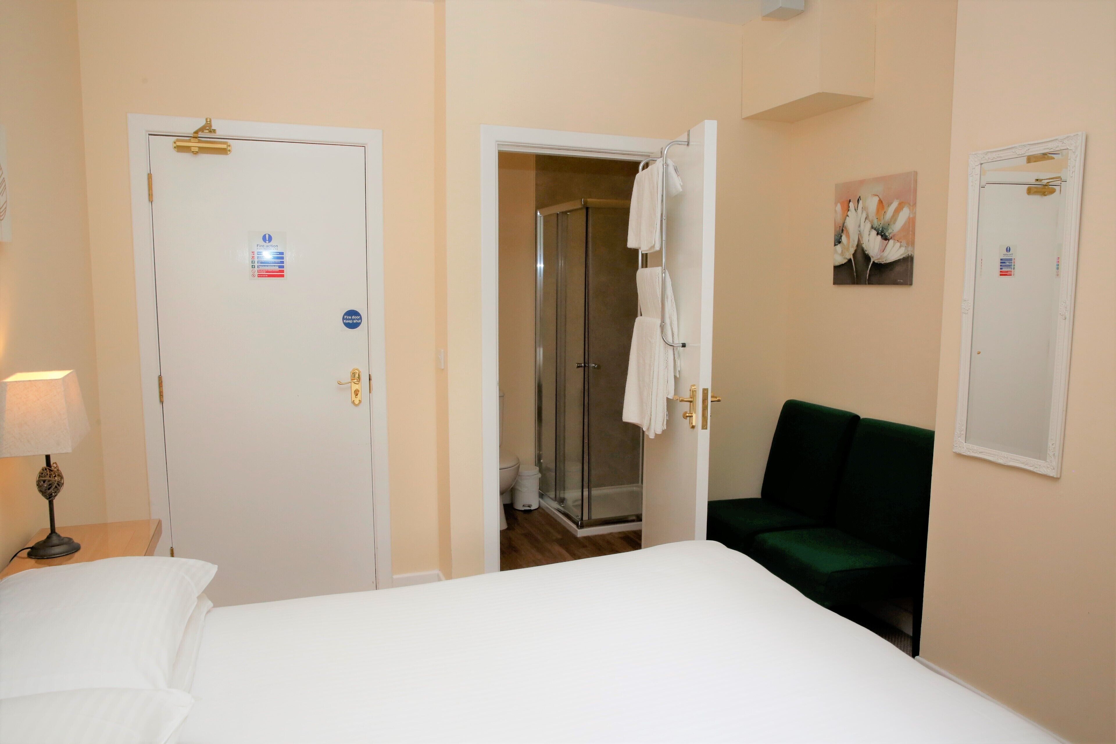 Habitación de hotel con cama, sofá verde, ducha y puerta con una toalla colgada.