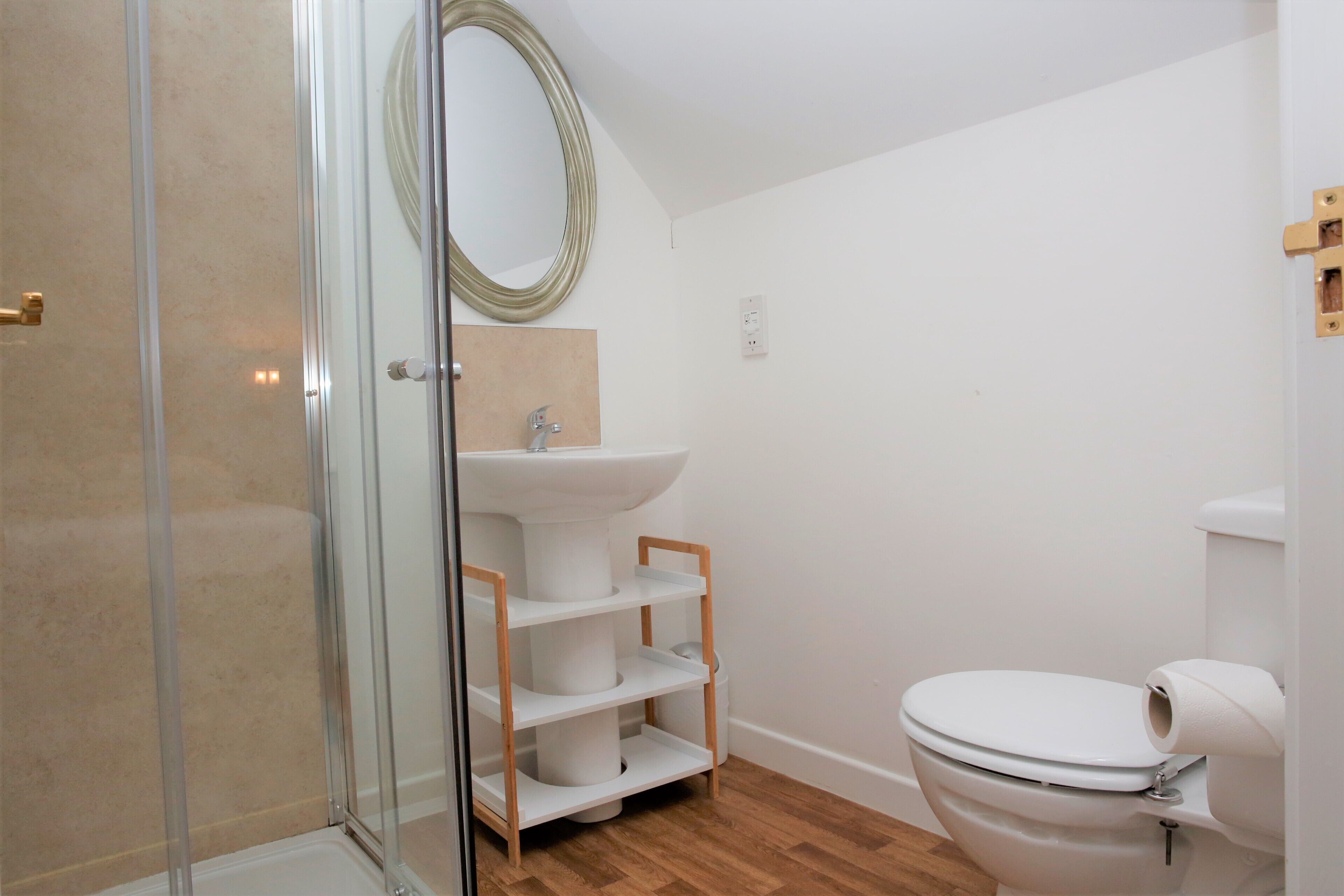A bathroom with a glass shower enclosure, a white sink, a toilet, and a wooden shelf unit.