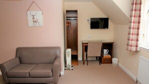 A cozy room with a brown sofa, a wooden desk, a television, and a plaid curtain. - Ardross Glencairn (Inverness)