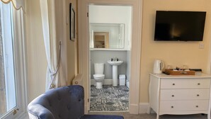 A room with a blue armchair, a white dresser, a television, and a bathroom visible through an open door. - Ardross Glencairn (Inverness)