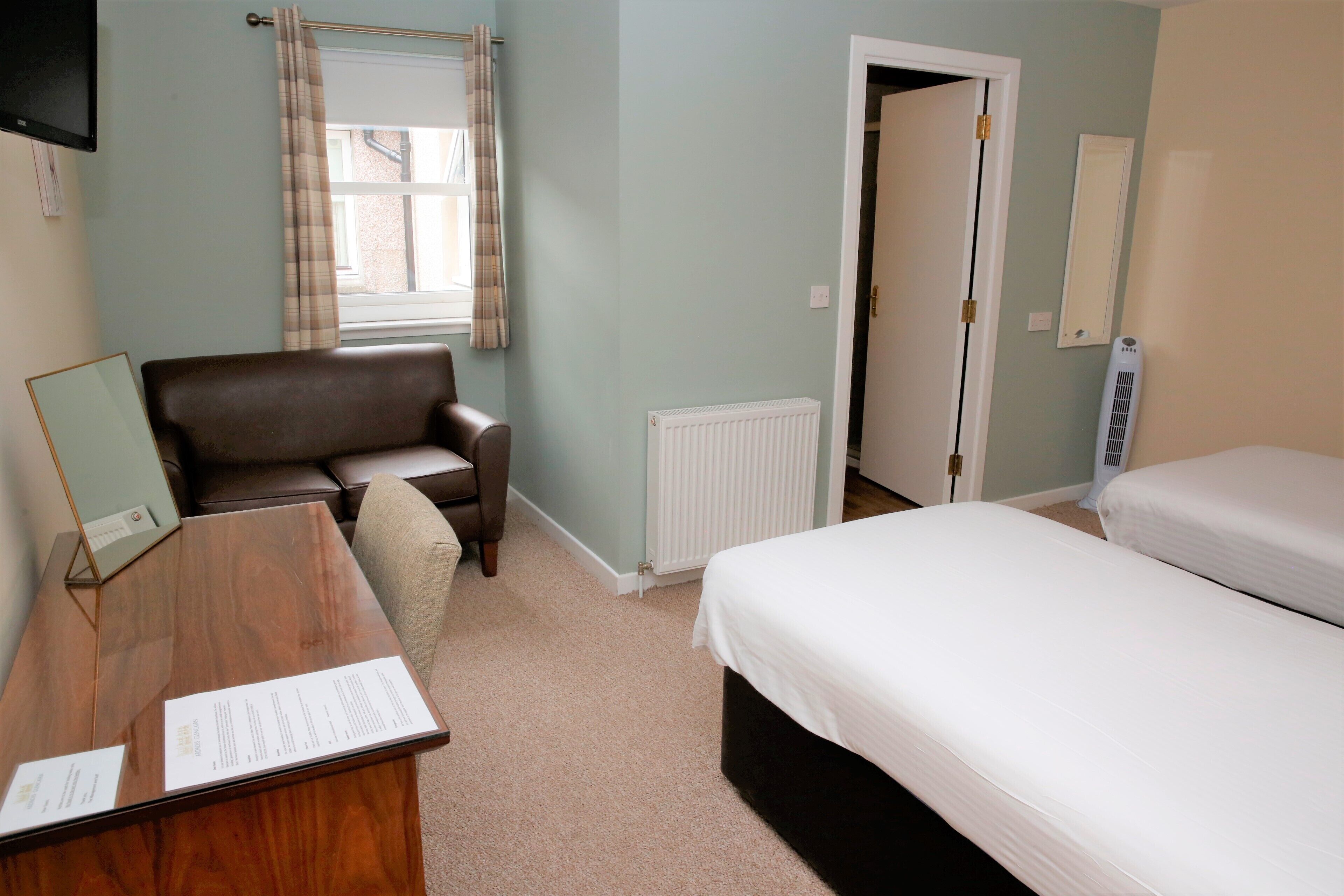 Een slaapkamer met een houten bureau, een bruine leren stoel, een bed, een radiator en een deur.
