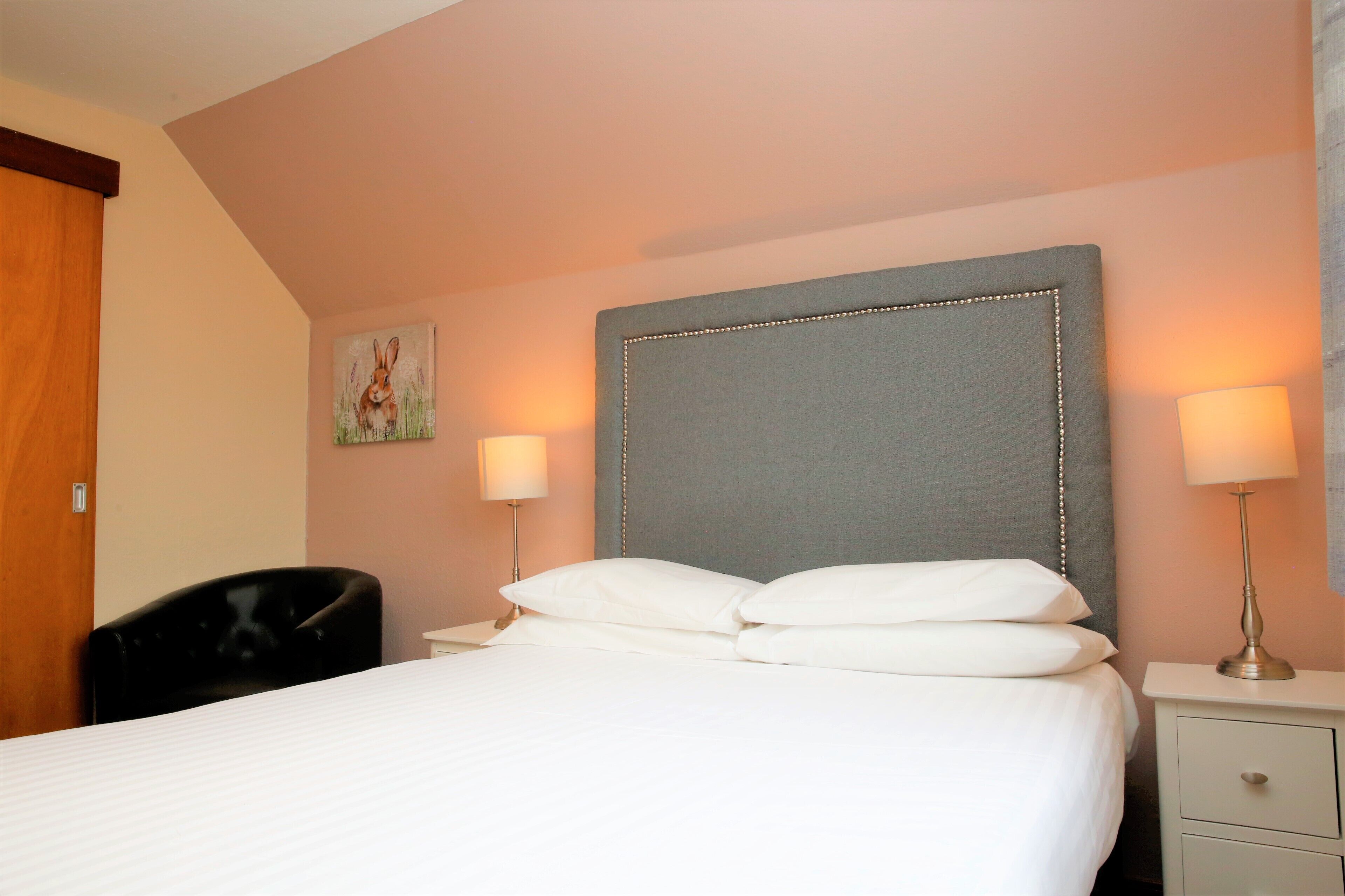 A neatly made bed with white linens, a grey upholstered headboard, and two bedside lamps.