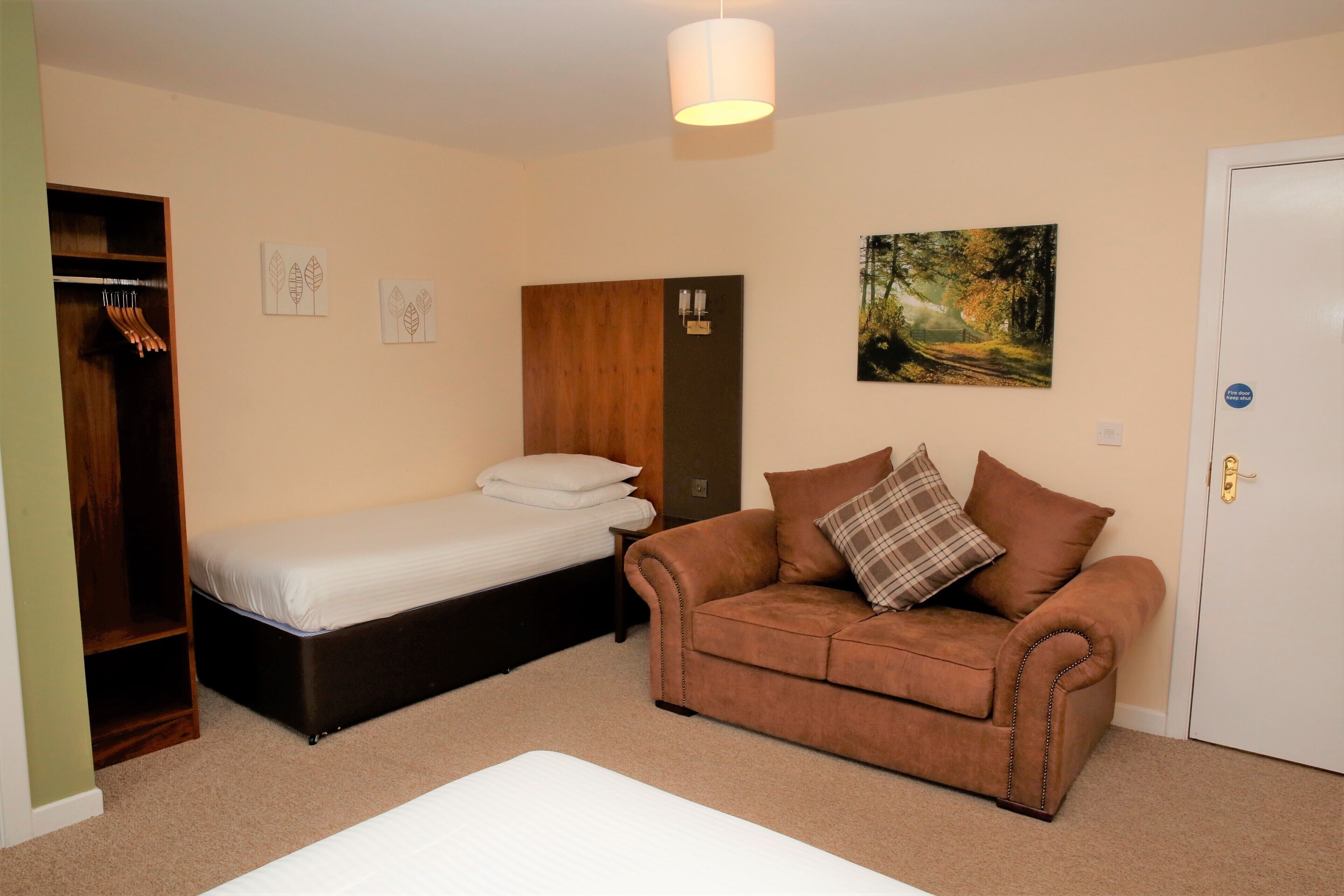 A bedroom with a bed, a brown sofa, a wardrobe, and a painting on the wall.