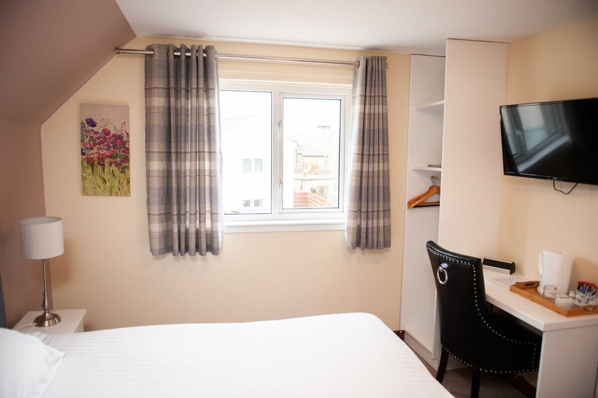 A hotel room with a bed, a desk, a chair, a TV, and a window with curtains.