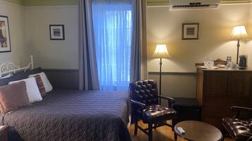 A hotel room with a bed, two chairs, a small table, a desk with a lamp, and a coffee maker.
