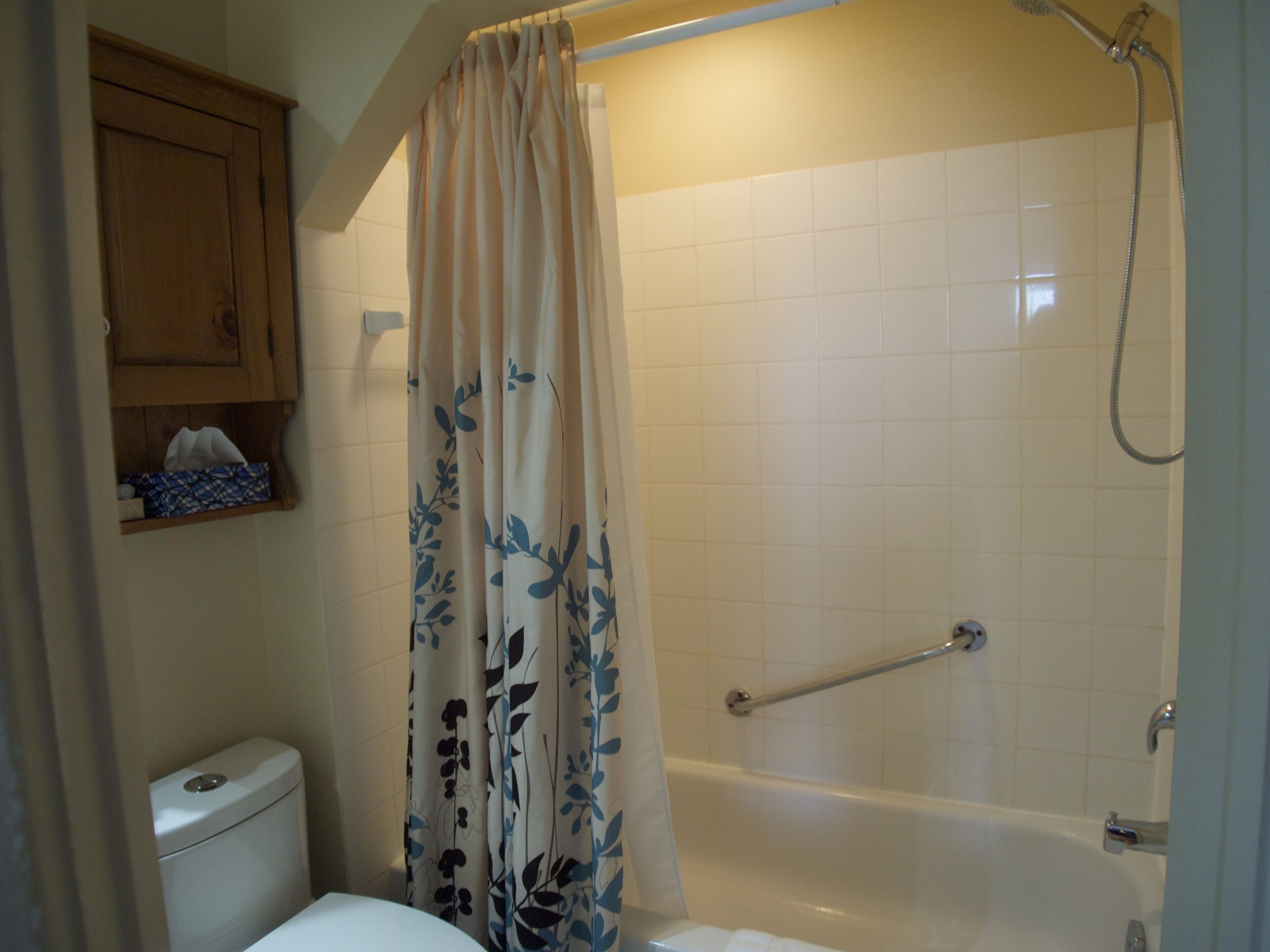 Un baño con inodoro, bañera, ducha y cortina con estampado floral.