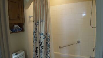 Un baño con inodoro, bañera, ducha y cortina con estampado floral.