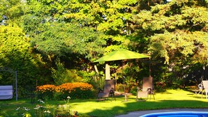 A backyard with a swimming pool, a covered seating area, and a lawn with flowers. - Au Manoir de la rue Merry (Magog)