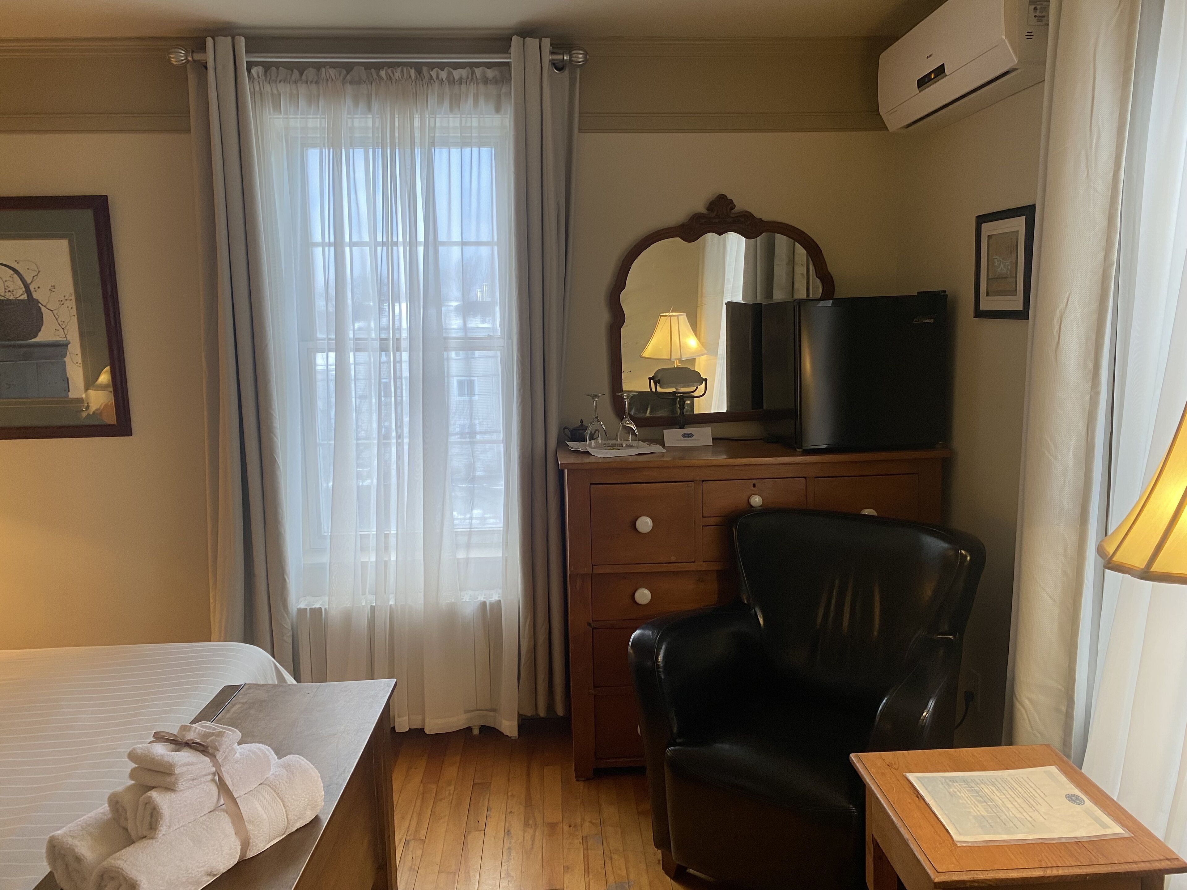 Una habitación de hotel con una cama, un escritorio con lámpara, una silla, un televisor y una ventana con cortinas.
