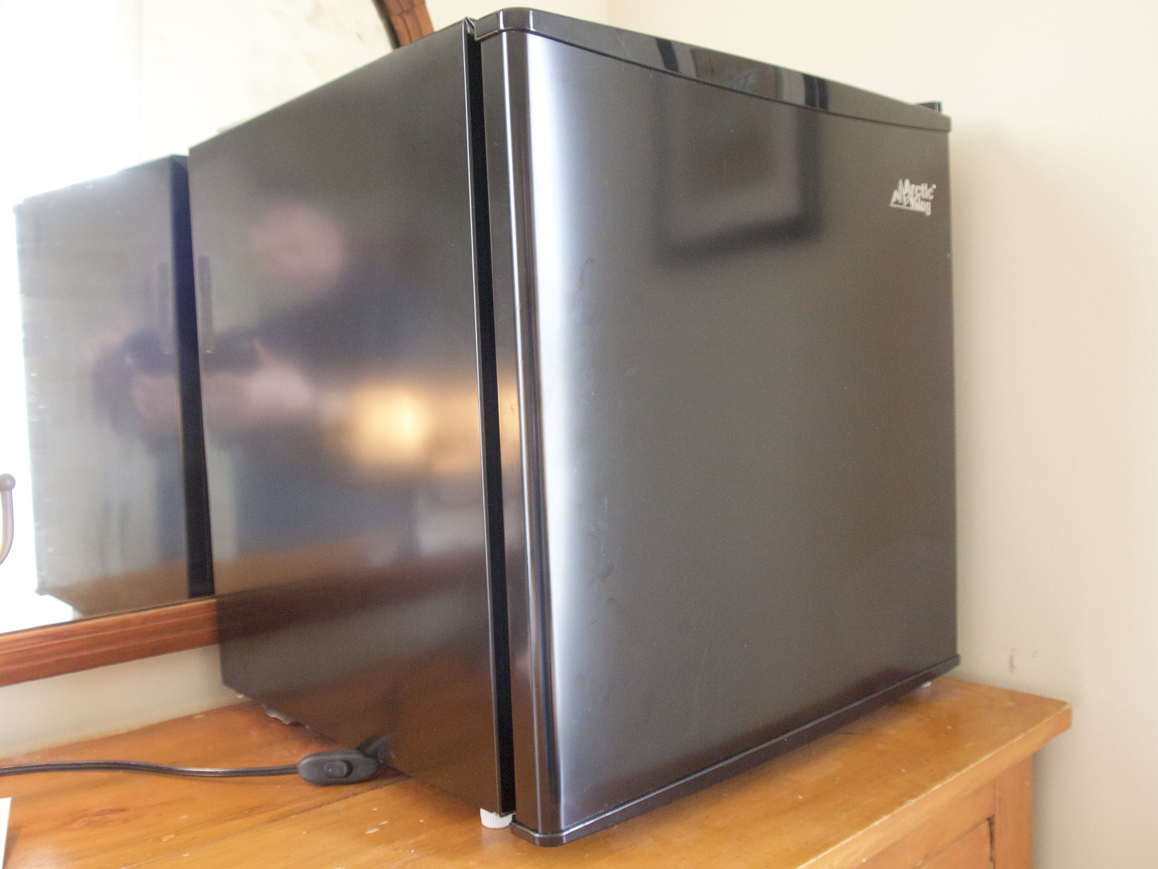 A black refrigerator with a control panel on the right side, placed on a wooden surface.