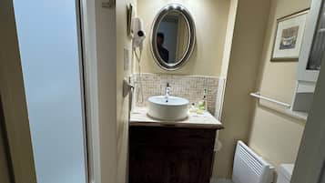 Une salle de bain avec des toilettes blanches, un lavabo avec un miroir au-dessus, un sèche-cheveux fixé au mur et un radiateur.