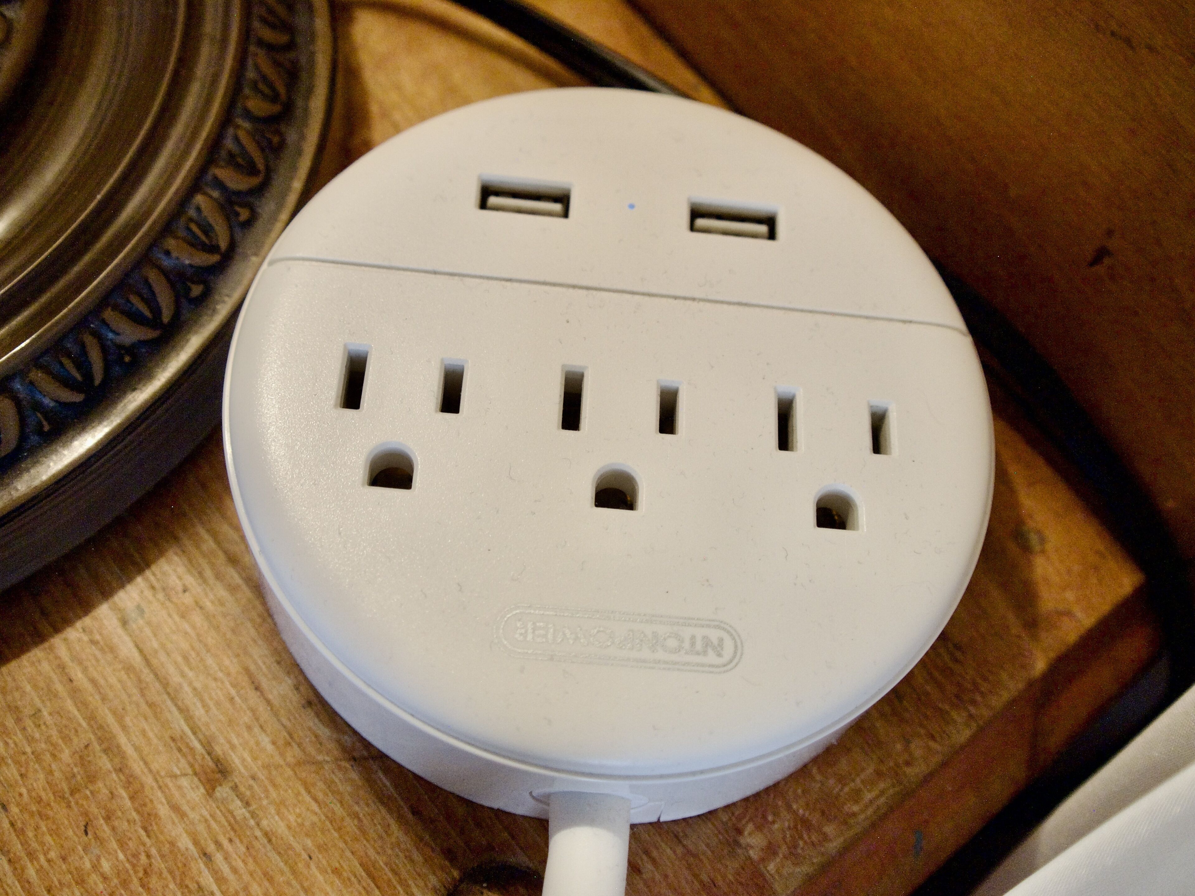A white power strip with multiple outlets and USB ports, placed on a wooden surface.