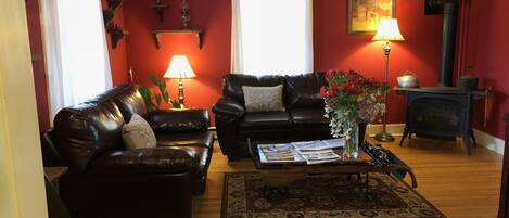 Una sala de estar con un sofá de cuero negro, una mesa de centro con revistas, un florero con flores, una chimenea y una pared roja.