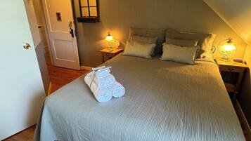 A cozy bedroom with a large bed, two bedside tables with lamps, a wooden ceiling, and a door leading to another room.