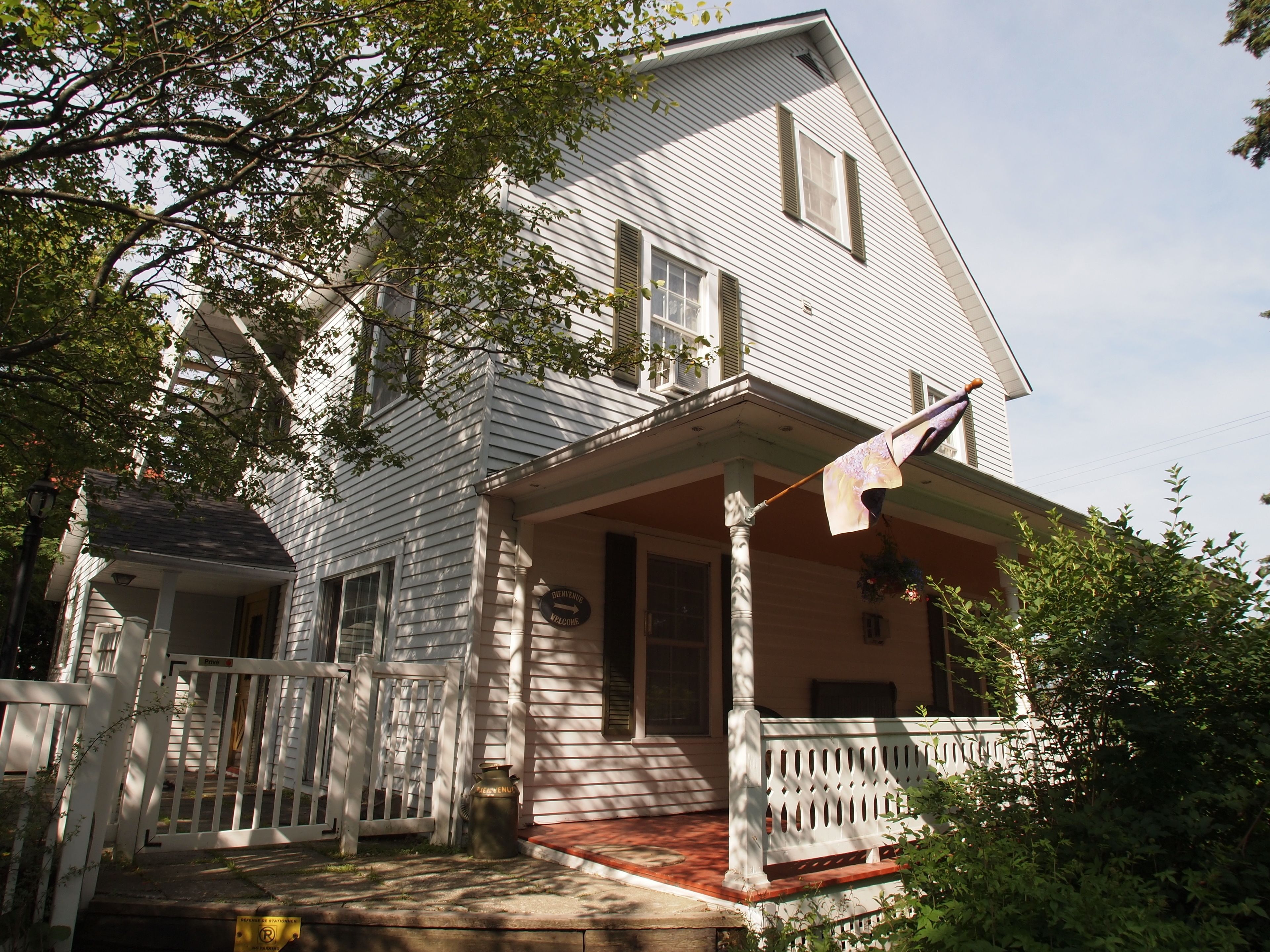 A white two-story house with a porch, a welcome sign, and a mailbox.