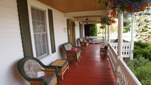 A porch with wicker furniture, a red floor, and white railings. - Au Manoir de la rue Merry (Magog)