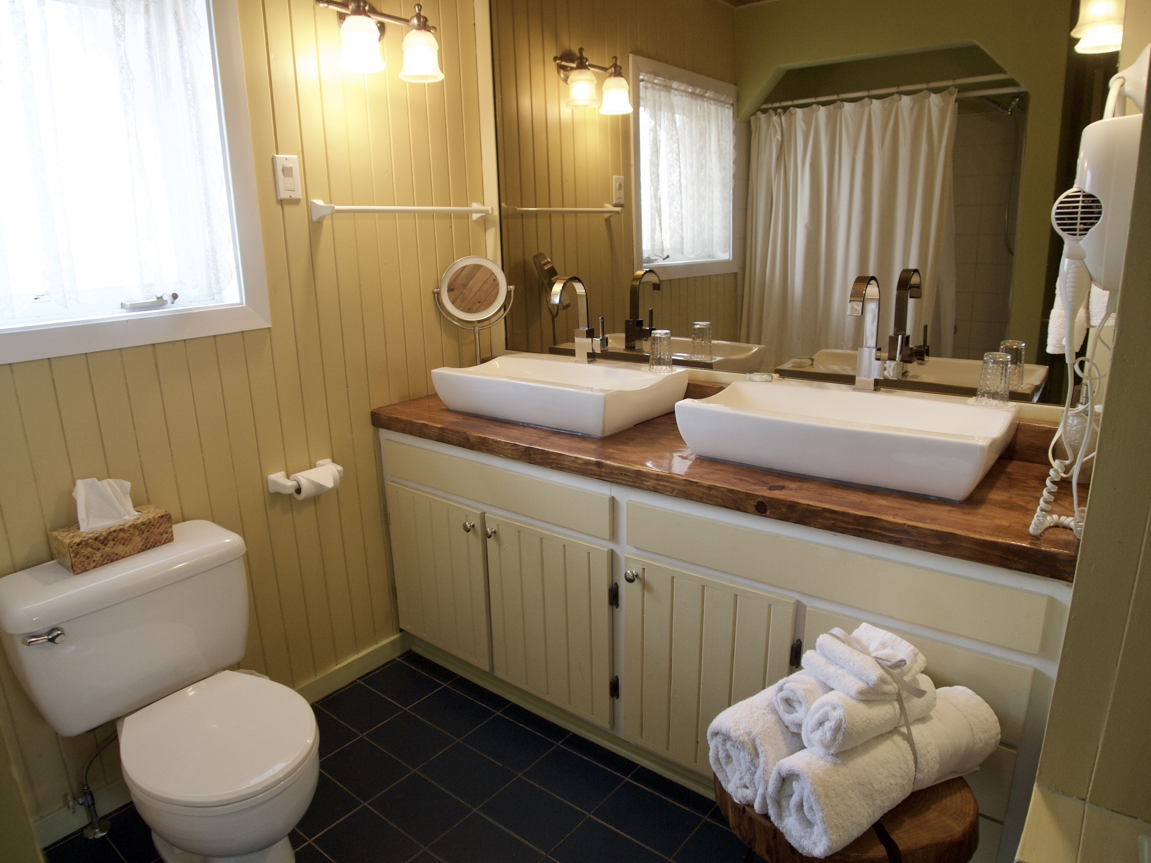 A bathroom with two sinks, a toilet, a mirror, and a towel rack.
