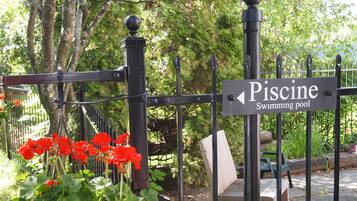 A sign for the Piscine swimming pool, surrounded by a metal fence and red flowers.