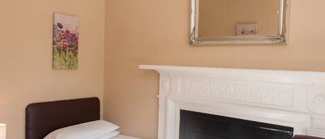 Un dormitorio con una cama, una chimenea blanca, un espejo y un cuadro en la pared.