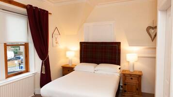 A bedroom with a bed, two bedside tables, a window with curtains, a radiator, and a wall decoration.