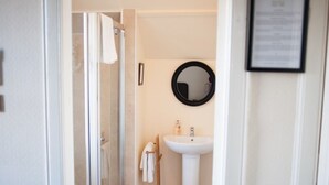 A bathroom with a glass shower enclosure, a white sink, and a round mirror on the wall. - Alban & Abbey House (Inverness)