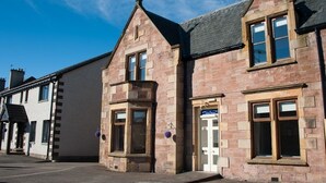 A traditional stone building with a pitched roof, a corner entrance, and a visible door. - Alban & Abbey House (Inverness)