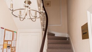 A staircase with a chandelier, a bulletin board, and a sign indicating room 12. - Alban & Abbey House (Inverness)