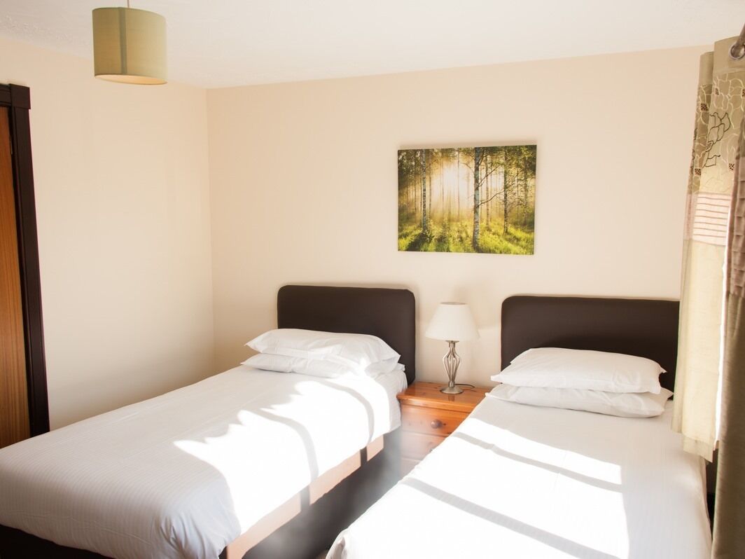 Ein Hotelzimmer mit zwei Einzelbetten, einem Nachttisch mit Lampe und Wandbild mit Waldmotiv.