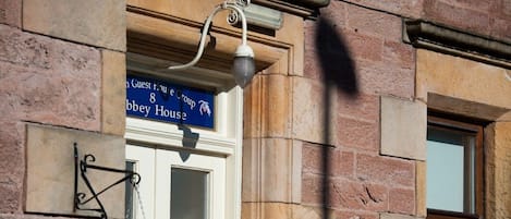 A building facade with a sign reading "Guest House" and a hanging purple flower.