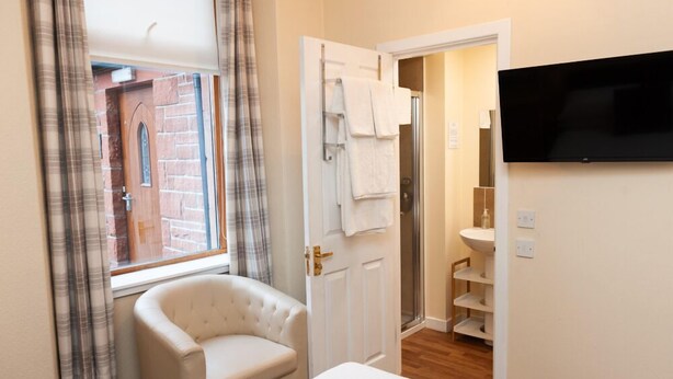 A hotel room with a bed, a chair, a TV, a bathroom with a shower, and a window with curtains. - Alban & Abbey House (Inverness)