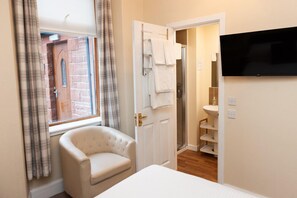 A hotel room with a bed, a chair, a TV, a bathroom with a shower, and a window with curtains. - Alban & Abbey House (Inverness)