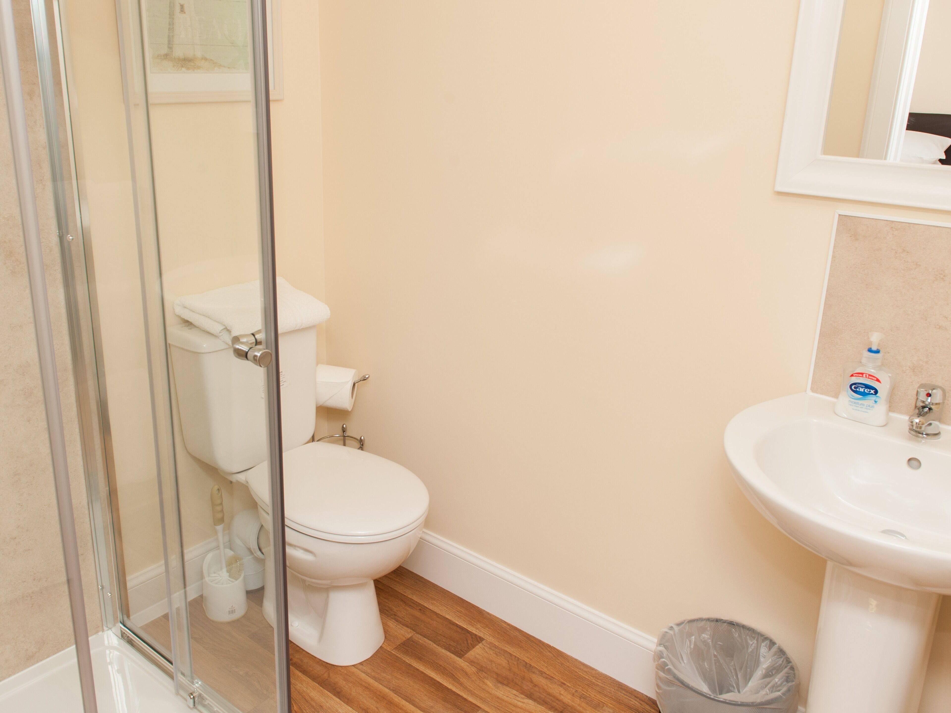A bathroom with a toilet, a glass shower enclosure, a sink, and a trash bin.