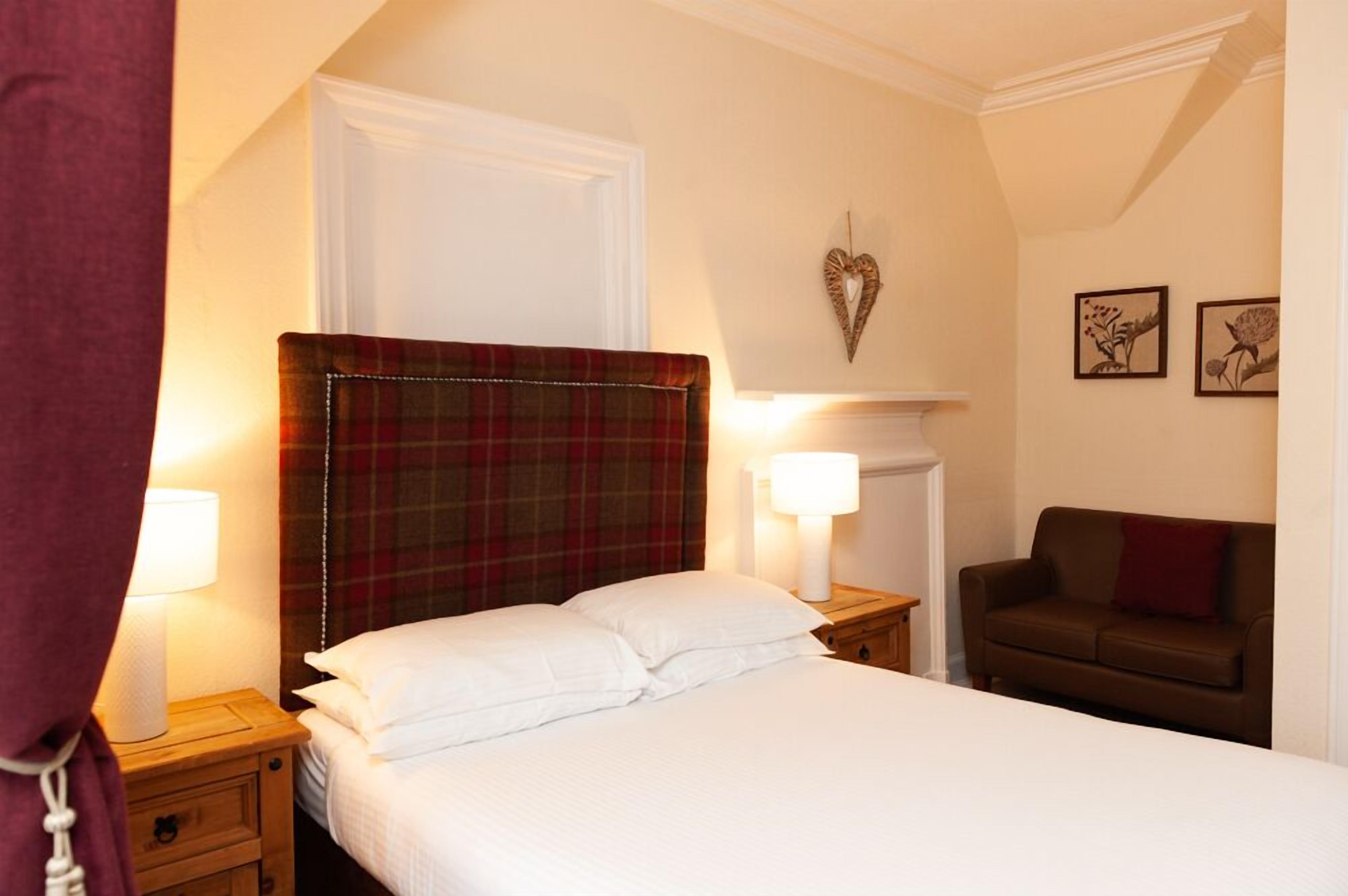 Una habitación de hotel con una cama, dos mesitas de noche con lámparas, un sofá marrón y una decoración con forma de corazón en la pared.