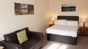 A bedroom with a bed, two bedside tables with lamps, a dark leather sofa, and two wall-mounted paintings.